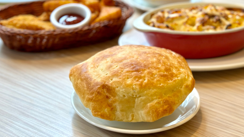 A small dish topped with baked puff pastry on a table, more food in the background.