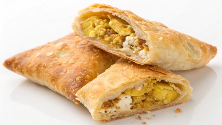 Samosas styled isolated on a white background, one cut open to show the filling.