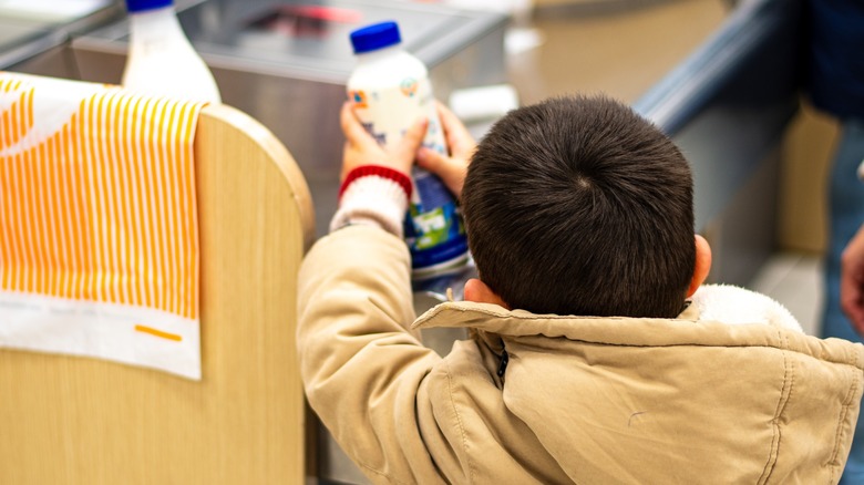 Little Child Placing a Bottle of Milk on the Supermarket Checkout Counter