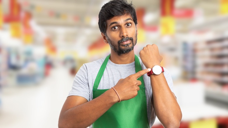 Grocery employee pointing at watch to indicate time