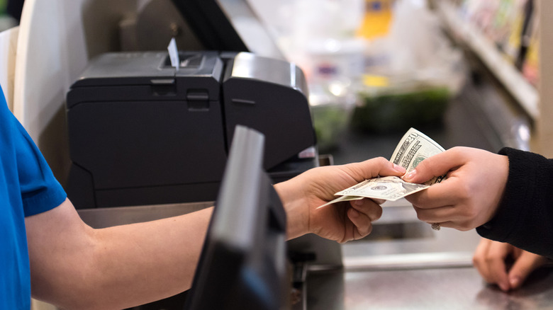 Person paying for groceries at the supermarket checkout, handing cash money to the cashier