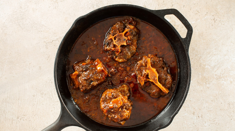 A top down view of braised oxtails in a cast iron skillet.