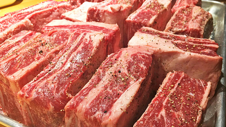 Seasoned raw beef short ribs on a baking pan ready to put into the oven.