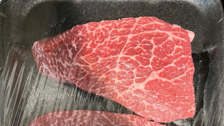 A bottom round cut of steak within a black styrofoam package.