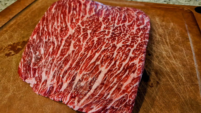 A bottom sirloin cut of beef resting on a wooden cutting board.