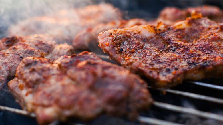 Several chuck steaks are cooking on a grill.