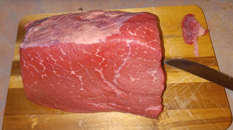 A raw cut of cross rib beef rests on a wooden cutting board, a knife sitting to the right.