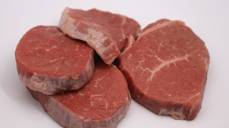 Several eye of round steaks piled together with a white background.