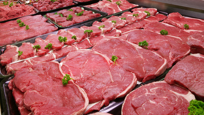 Several different cuts of beef in the refrigerated section at a grocery store.
