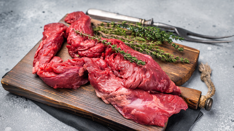 Raw beef skirt steak resting on a wooden cutting board, herbs to the right.