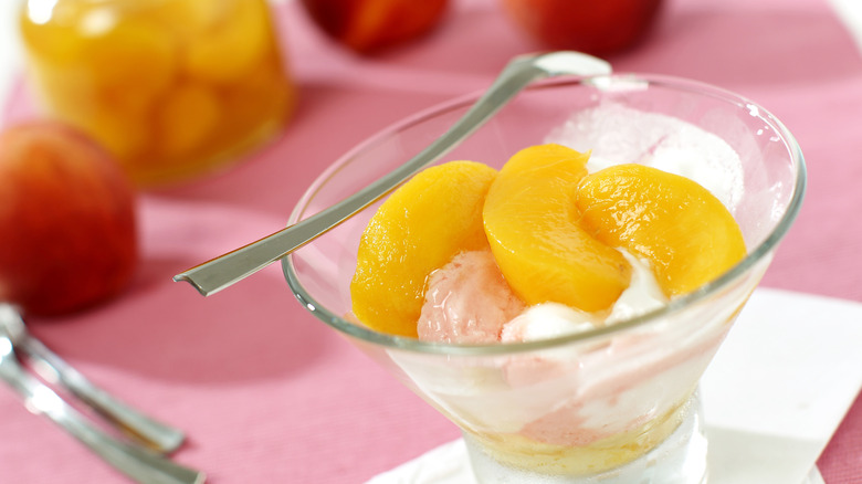 A glass filled with ice cream and canned peaches on a pink background