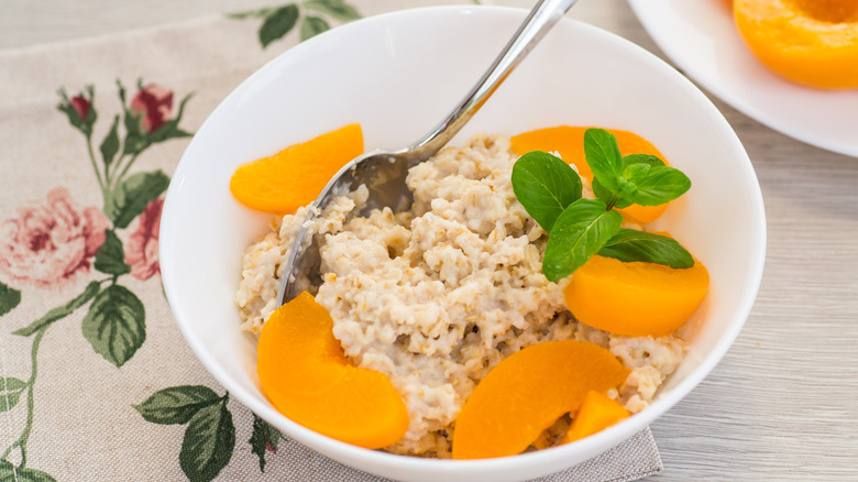 A bowl of oatmeal with canned peaches and mint