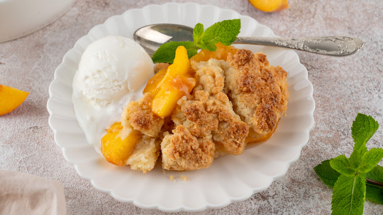 A serving of homemade peach cobbler on a plate with ice cream and mint
