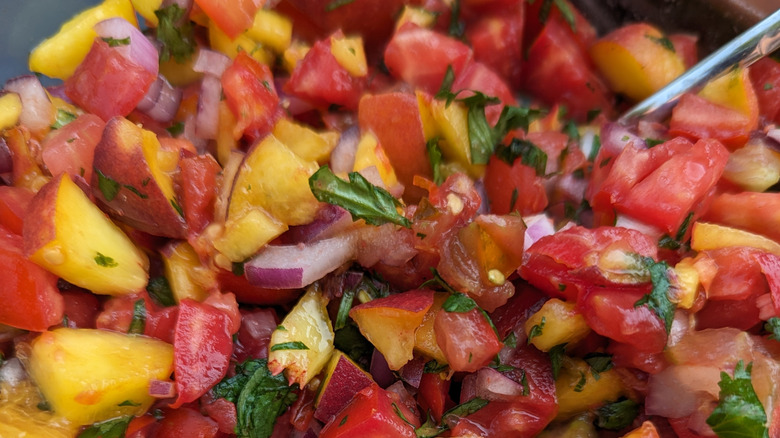 A close-up of chunky fruit salsa featuring heirloom tomato, red onion, cilantro, and peach