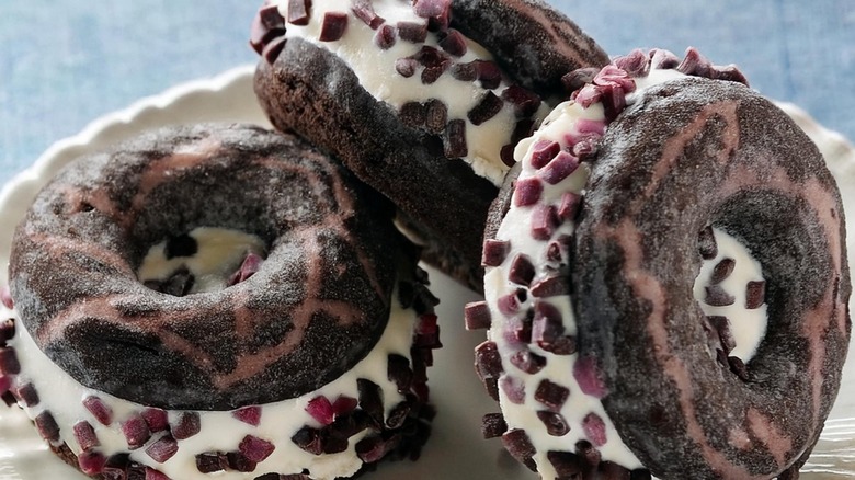Three dark brown donut ice cream sandwiches on a plate.