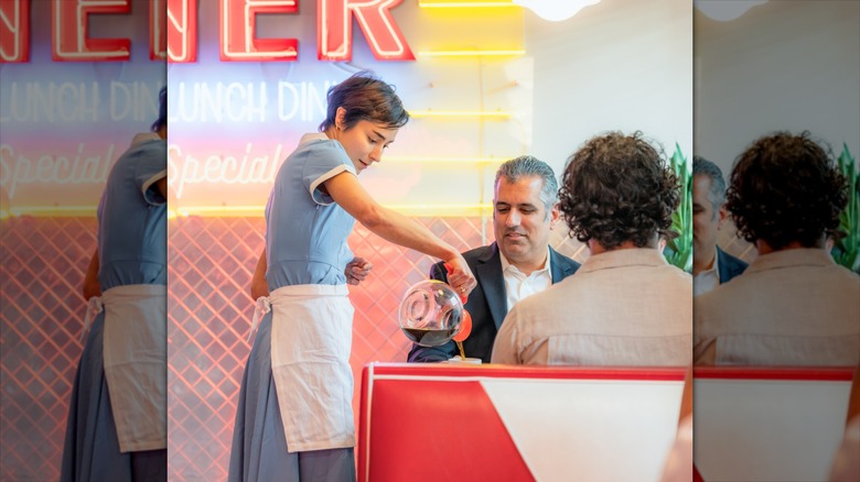 A diner waitress pouring refill coffee from a flask for a customer at a traditional American diner