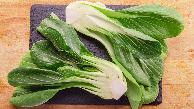 Two heads of bok choy rest on a cutting boad on a wooden table.