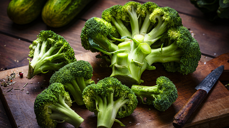Heads of broccoli rest on a cutting board. A knife rests on the board in the right corner.
