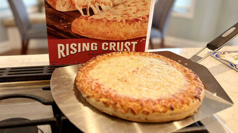 A rising crust four cheese DiGiorno pizza on a pizza peel