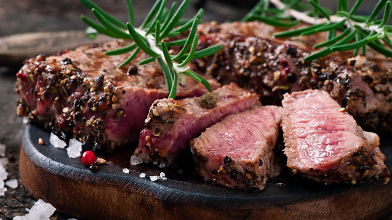 A plate of juicy sliced steak crusted in peppercorns and garnished with rosemary