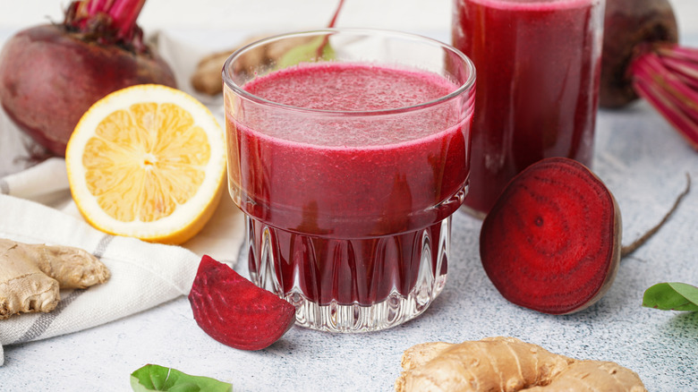 Glasses of fresh beet juice next to half a lemon, fresh beet, and whole ginger