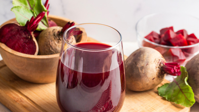 Glass of fresh beet juice on a wooden board next to bowls of whole and cubed beets