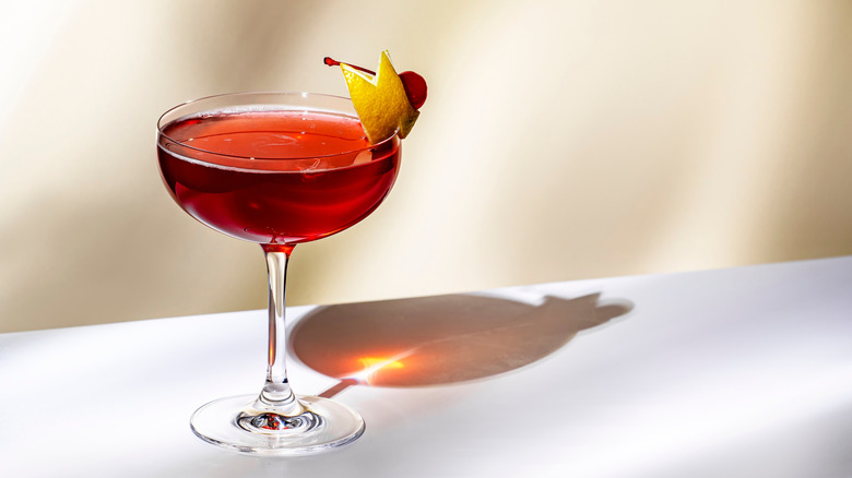 A red cocktail in a martini glass with a citrus and cherry garnish
