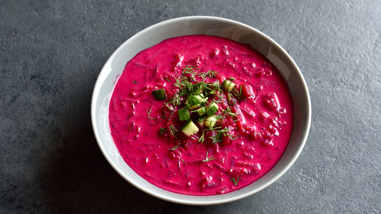 A bowl of beet soup in a white bowl garnished with fresh herbs and veggies