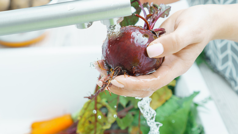 A person rinsing a beet in a sink above other fresh produce