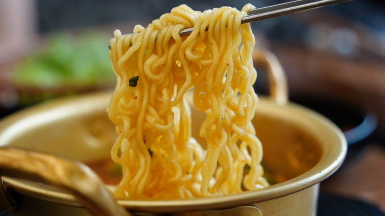 Instant ramen noodles in a traditional pot, lifted with chopsticks