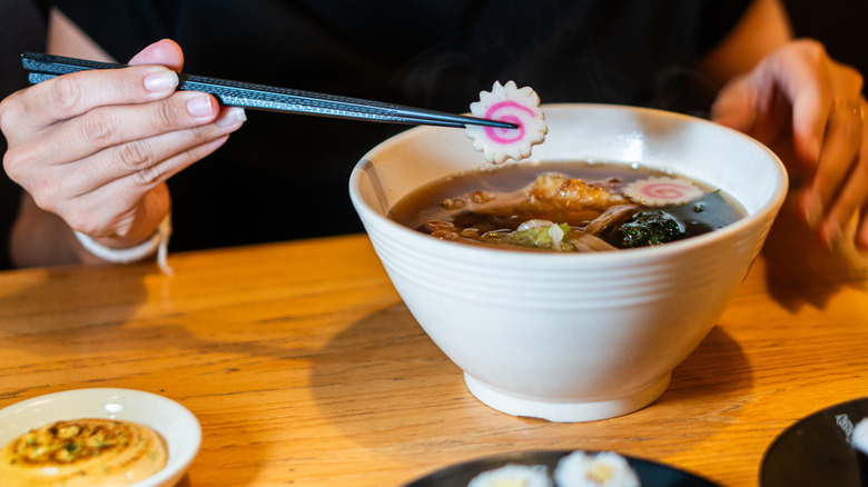 A person holding chopsticks over a bowl of ramen