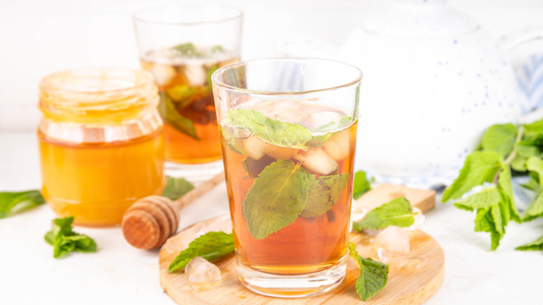 Mint and honey iced tea drink on a wooden board with a jar of honey and a dipper in the background