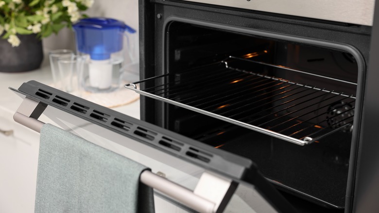 Partially open electric oven with kitchen towel hanging on the handle