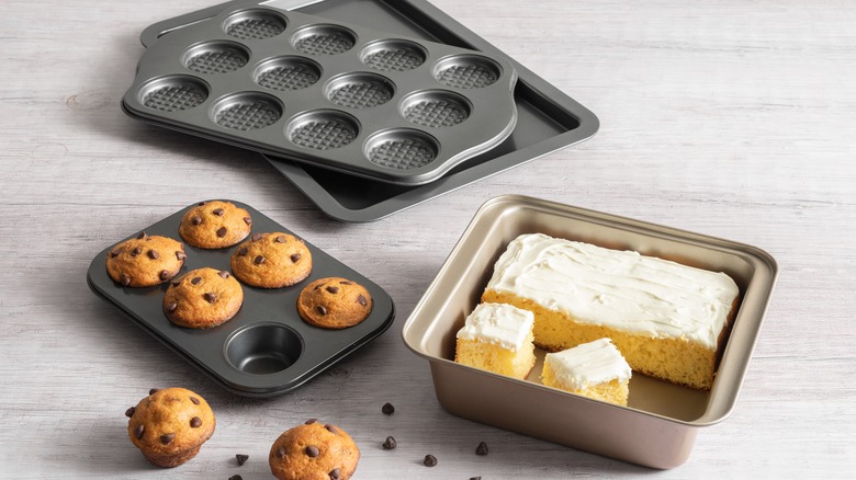 Square baking pan containing cake, muffin tin with muffins, other assorted baking pans