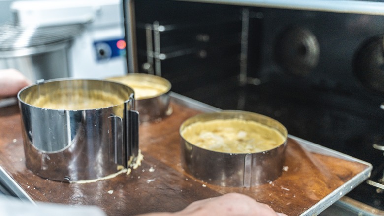 Apple tarts in molds being placed in a convection oven to bake
