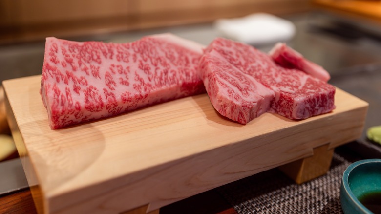 Raw A5 Kobe beef with intense marbling presented on a wooden board at a Japanese teppanyaki restaurant ready for high-end steak preparation