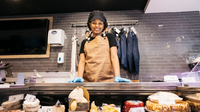 Young butcher shop worker smiling behind the counter of a gourmet supermarket