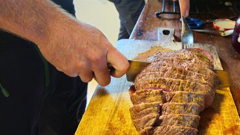 Juicy moose steak being sliced on a wooden cutting board, showing a golden crust and tender pink center.