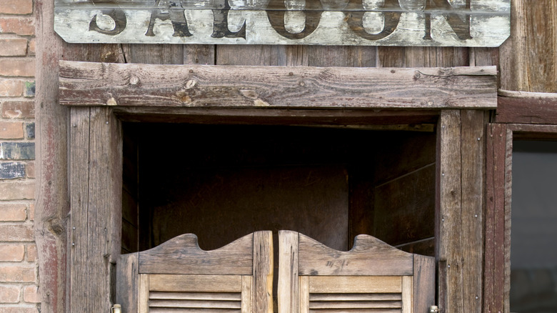 The store front of a saloon, with wooden swinging doors. A sign reads saloon overtop of the doors.