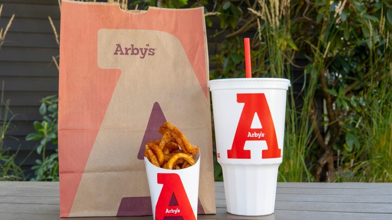 Arby's bag next to glass of cola and curly fries.