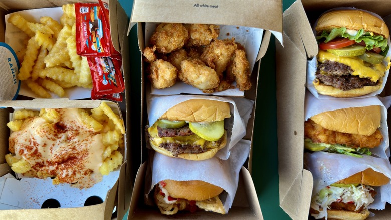 A large assortment of Shake Shack fast food items—cheeseburgers, fried chicken sandwiches, fries, and chicken nuggets