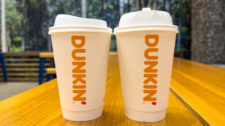 Two Dunkin' hot coffee cups on a wood table outside.