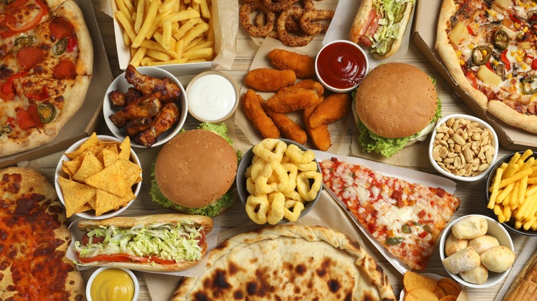 Various fast food items including pizza, burgers, wings, and fries on a wood table.