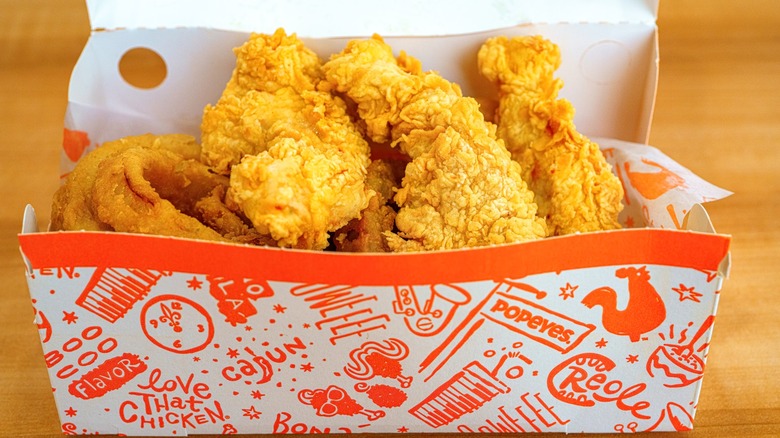 Paper box holding Popeyes chicken on a wood table.