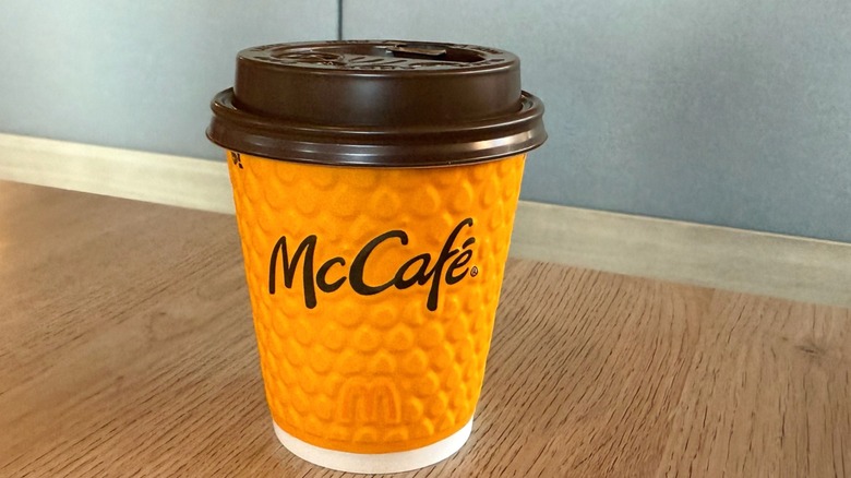 A vibrant orange McCafe cup sits on a wooden table