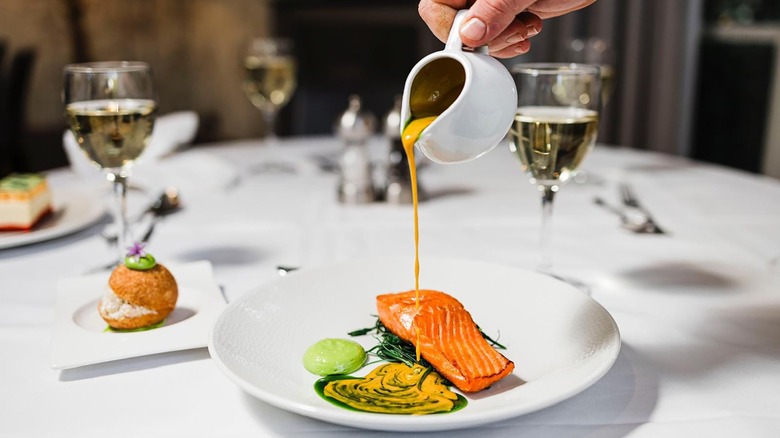 Fine dining image of pouring sauce over salmon dish