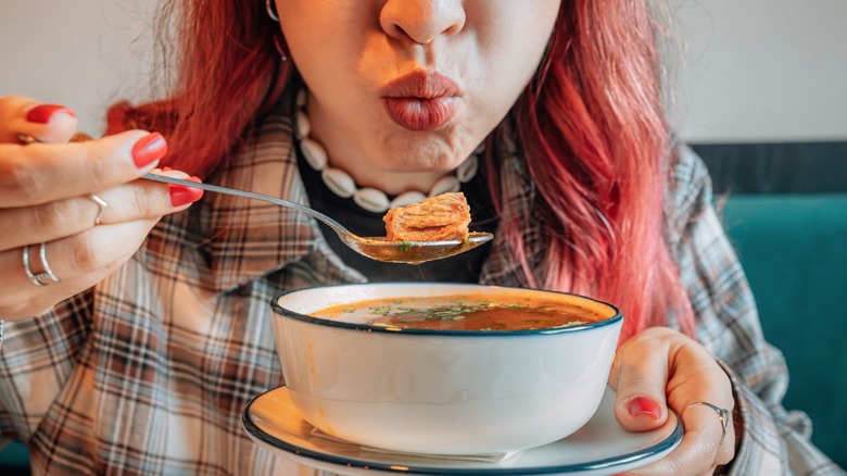 young woman blowing on spoonful of soup to cool it down