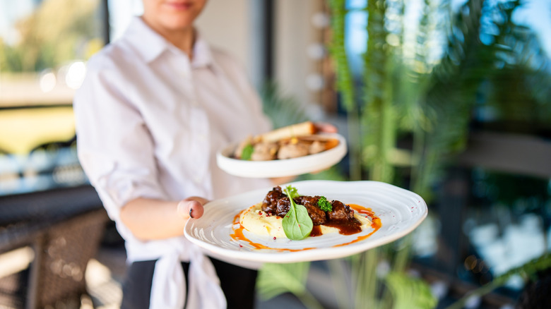 Server holding two plates out to the camera