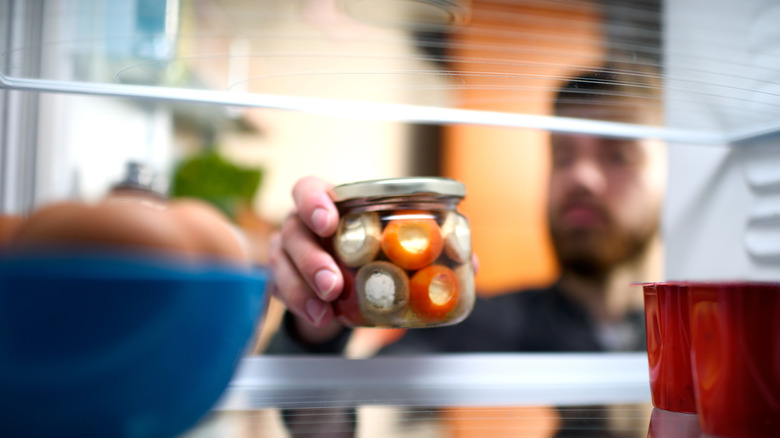Man putting jar of peppers in fridge