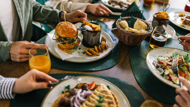 large table with diners gathered around big meals and plates of food like hamburgers